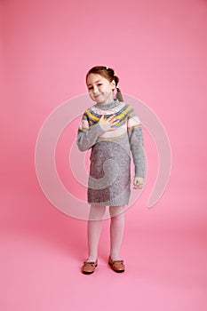 Portrait of little funny smiling girl showing to themself in warm dress on rosa background