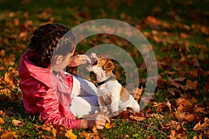 Portrait of a little girl on a background of blurred orange leaves in an autumnal sunny day.