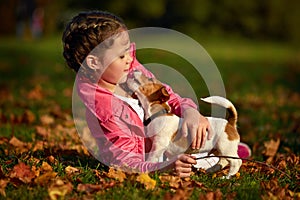 Portrait of a little girl on a background of blurred orange leaves in an autumnal sunny day.