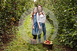 Portrait of little girl and beautiful mother in organic apple orchard happy and having fun