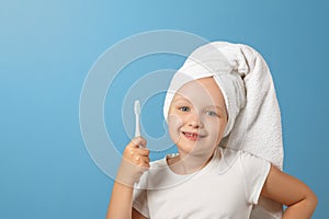 Portrait of a little girl on a blue background. A child with a white towel on his head holding a toothbrush. The concept of daily