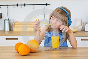 Portrait of a little girl in a blue dress drinks an orange juice and thinks