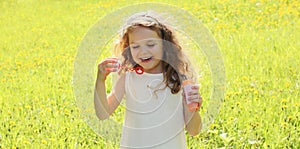 Portrait little girl child blowing soap bubbles in summer day