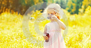 Portrait of little girl child blowing soap bubbles in sunny summer day