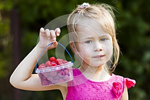 Portrait of a little girl child holdind small basket of ripe raspberries. Close-up