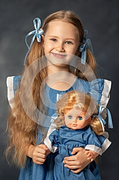 Portrait of little girl child kid holding and embracing her doll isolated on grey background. Child and favorite toy