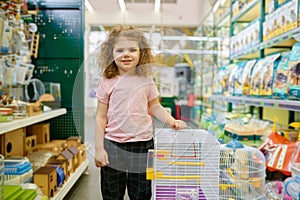 Portrait of little girl child standing nearby cage for rodent at pet shop