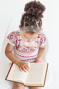 Portrait of a little girl in a colorful dress reading a book on a white background
