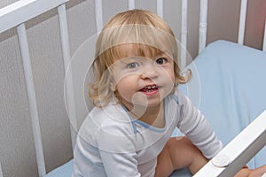 Portrait of a little girl in a crib. Childlike spontaneity, funny face, happy and cheerful look. Good health and mood.