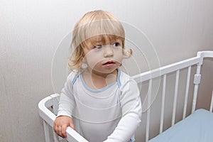 Portrait of a little girl in a crib. Childlike spontaneity, funny face, happy and cheerful look. Good health and mood.