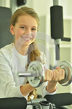 Portrait of little girl doing exercises with dumbbell in gym