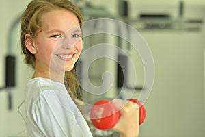 Portrait of little girl doing exercises with dumbbell in gym