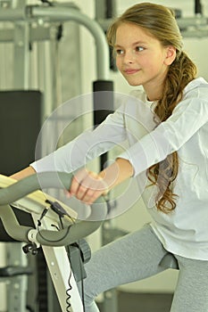 Portrait of little girl doing exercises on exetcise bike in gym