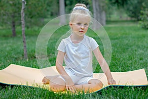 Portrait of little  girl doing yoga in in green grass.Child doing exercise on platform outdoors.