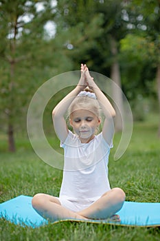 Portrait of little  girl doing yoga in in green grass.Child doing exercise on platform outdoors.