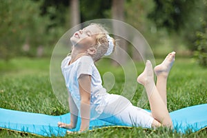 Portrait of little  girl doing yoga in in green grass.Child doing exercise on platform outdoors.