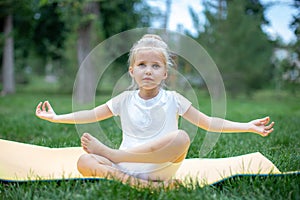 Portrait of little  girl doing yoga in in green grass.Child doing exercise on platform outdoors.