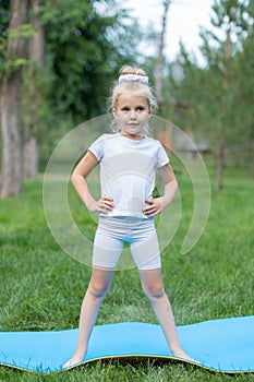 Portrait of little  girl doing yoga in in green grass.Child doing exercise on platform outdoors.