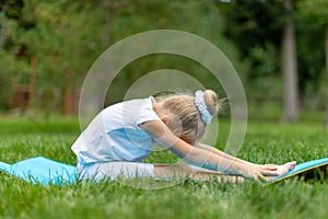 Portrait of little  girl doing yoga in in green grass.Child doing exercise on platform outdoors.