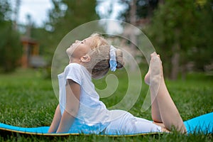Portrait of little  girl doing yoga in in green grass.Child doing exercise on platform outdoors.