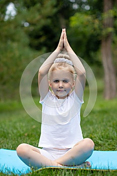 Portrait of little  girl doing yoga in in green grass.Child doing exercise on platform outdoors.