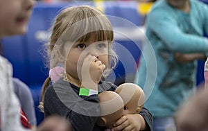 Portrait of a little girl with dolls picking her nose with her finger. Childish thoughtfulness and spontaneity.