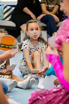 Portrait of a little girl in a dress sitting on the floor surrounded by children listening attentively