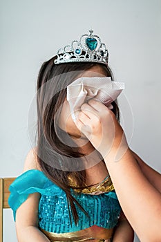 Portrait of a little girl dressed in arabian princess costume while hand pressing tissue on face. Wiping nose.