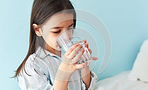 Portrait of a little girl drinking fresh water in the bed at home. Cute preschool kid holding glass of pure water in the morning.