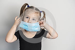 Portrait of a little girl of European appearance in a disposable mask with two ponytails. girl takes off the mask with her hand