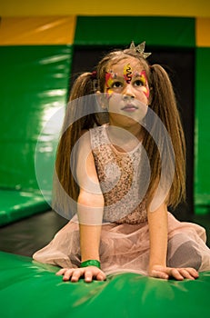 Portrait of a Little girl with facepainting makeup on her face on a trampoline playground in kids play room