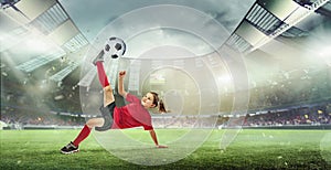 Portrait of little girl, football player in red uniform hitting ball and falling isolated over open air stadium.