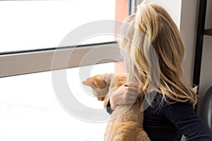 Portrait of a little girl with a ginger cat together looking out the window