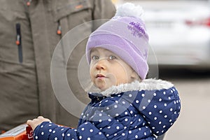 Portrait of a little girl in a hat sitting in a grocery stroller next to her grandfather. Concept: refugees from Ukraine, assistan
