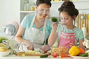 Portrait of little girl with her mother cooking together at kitchen table