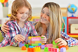 Portrait of little girl and her mother playing colorful plastic blocks together in her room