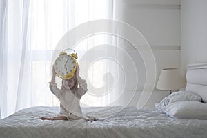 Portrait of little girl holding alarm clock over her head, isolated over white