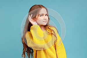 Portrait of little girl holding hand near ear and listening carefully intently to what you say.