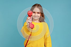 Portrait of little girl holding and showing retro phone handset to camera, asking to answer phone.