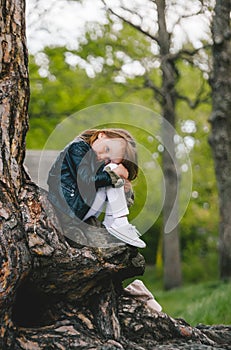 Portrait of little girl with long hair leaning on tree trunk at park in forest. Cute kid, nature lover concept