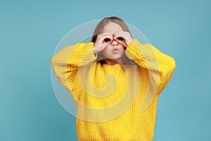 Portrait of little girl looking through fingers shaped like binoculars and expressing amazement.