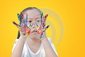 Portrait of little girl with looking through her colorful hands painted isolated on yellow background. Focus at child hands