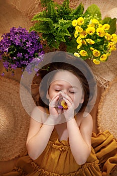 Portrait of a little girl lying on background from straw hats holding flowers in hands, summer and travel feeling concept