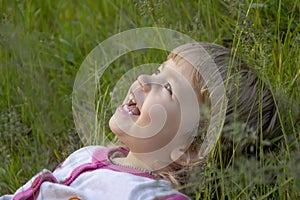 Portrait of a little girl lying on her back in the long grass and laughing.