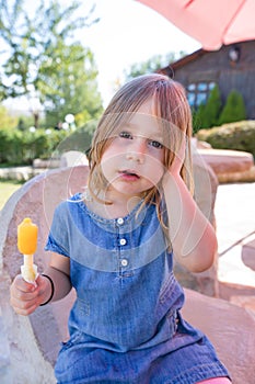 Portrait of little girl with orange ice lolly in park