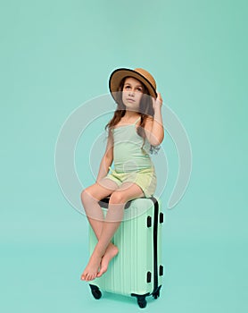 Portrait of a little girl, passenger sitting on a trendy plastic valise, looking at camera, isolated studio background