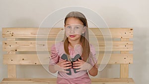 Portrait of little girl in a pink dress in the studio, she sits on wooden bench