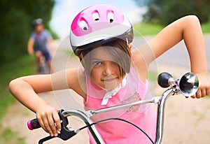 Portrait of a little girl in a pink safety helmet driving her bike.
