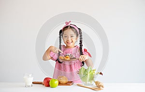 Portrait of little girl point to cake and stand in front of vegetables on table with white background