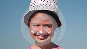 Portrait of little girl with protective sunscreen on nose and cheeks at beach